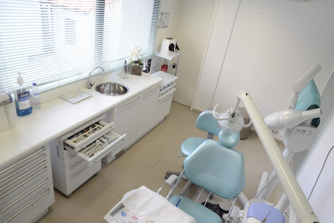 Cadeira odontológica verde-água e gaveteiros brancos na sala de atendimento