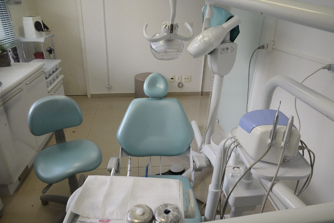 Sala de atendimento com cadeira odontológica e mocho verde-água