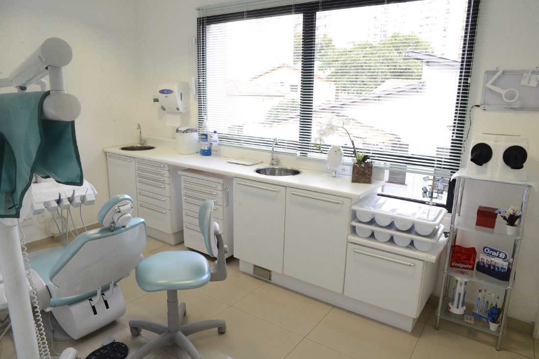 Sala de atendimento com janela ampla, bancada branca e cadeira verde-água
